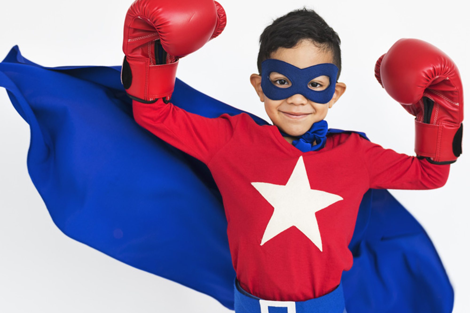 Little boy dressed as a superhero with red shirt and a white star, blue cape and mask, and red boxer gloves.