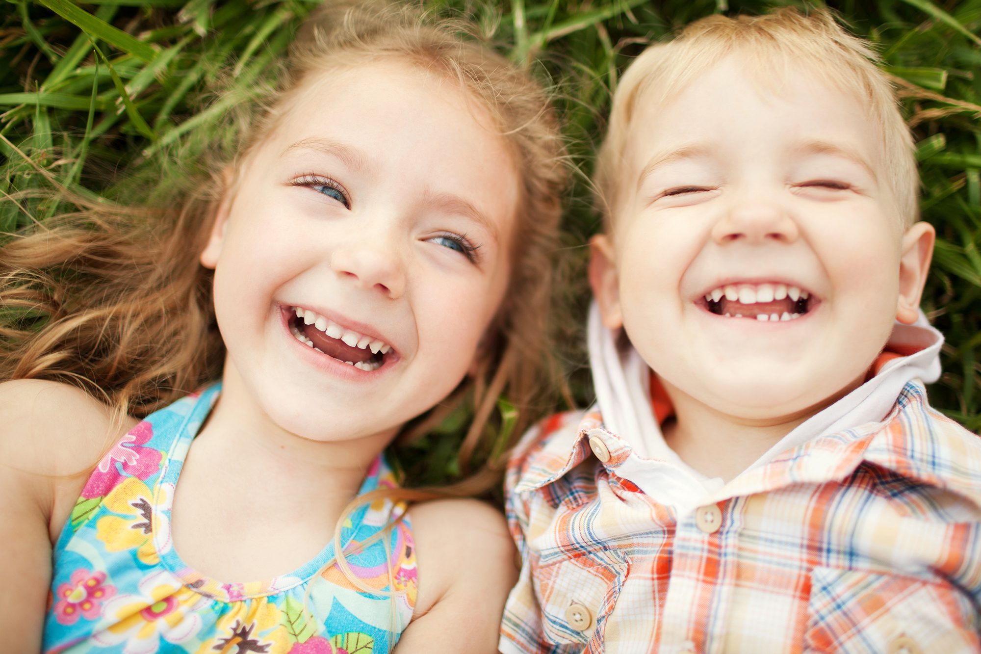 A girl and a boy laying on grass and laughing. 